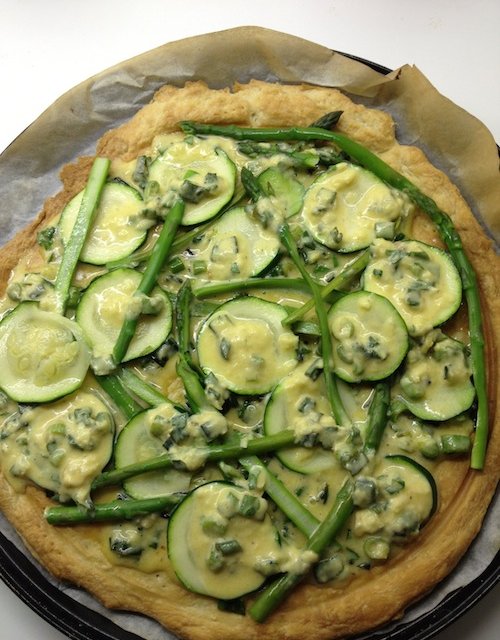 Haal de pizzabodem uit de oven, bestrijk met het eiermengsel, beleg met de kort gekookte courgette en asperge en besprenkel met de overgebleven saus en bestrooi met kaas.